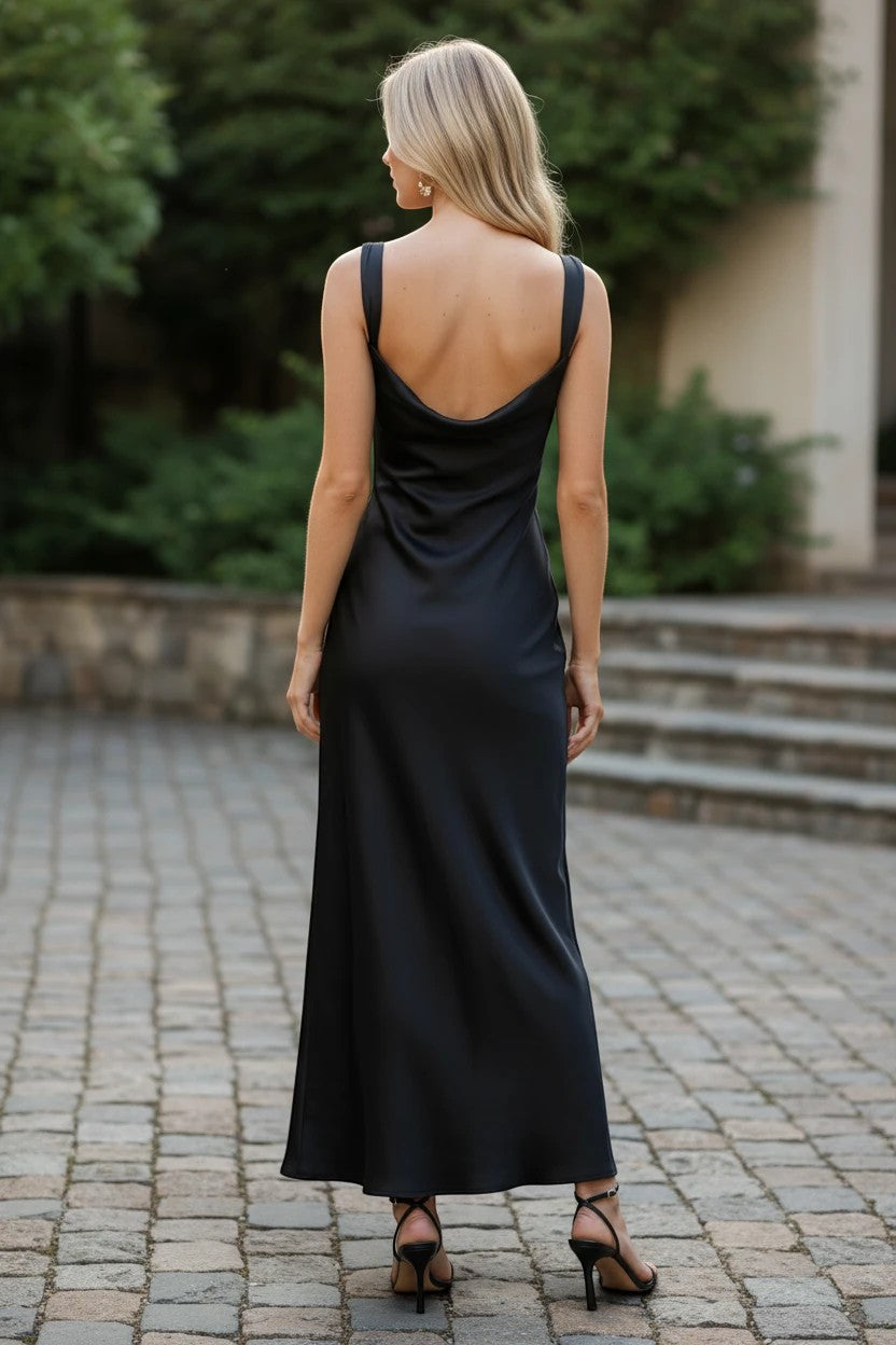 Robe de cocktail longue noire Valerelle à dos nu et coupe fluide portée par une femme en extérieur