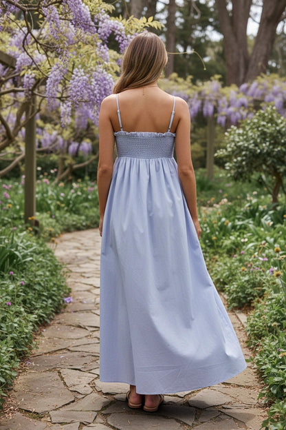 Robe longue Valerelle bleu clair à dos smocké portée par une femme dans un jardin fleuri