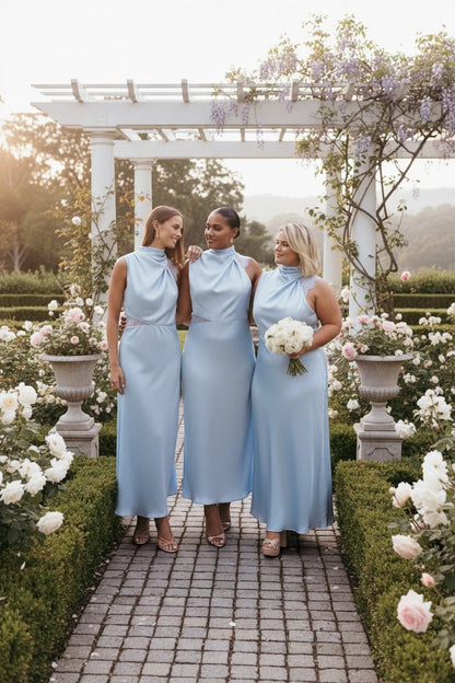 Trois femmes portent des robes longues Valerelle bleu ciel en dentelle à col licou dans un jardin fleuri.