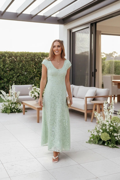 Femme portant une robe longue Valerelle en dentelle vert sauge avec encolure arrondie lors d'une réception en extérieur