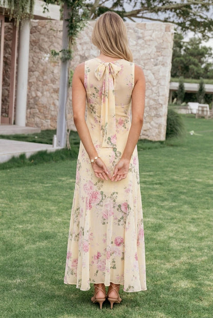 Vue arrière de la robe longue Valerelle jaune à imprimé floral avec nœud au dos, portée dans un jardin.