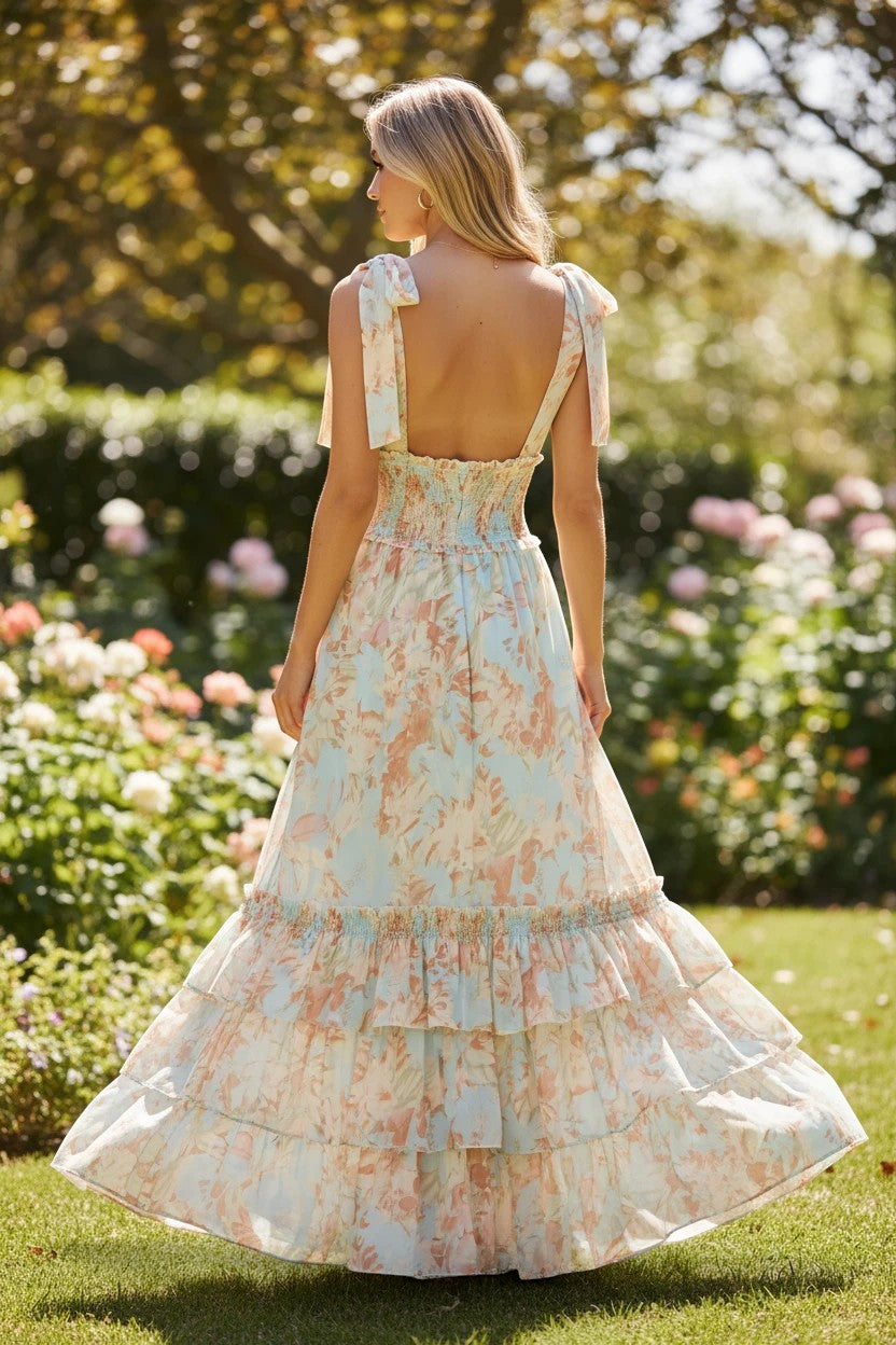 Robe longue Valerelle à volants et imprimé floral pastel, dos nu avec bretelles nouées, portée dans un jardin ensoleillé.