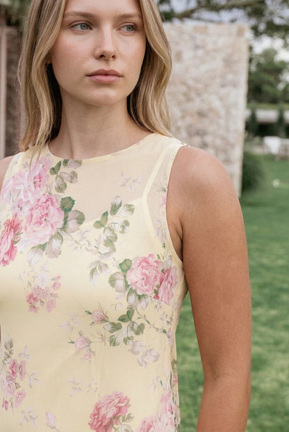 Robe longue Valerelle jaune à imprimé floral portée par une femme blonde dans un jardin