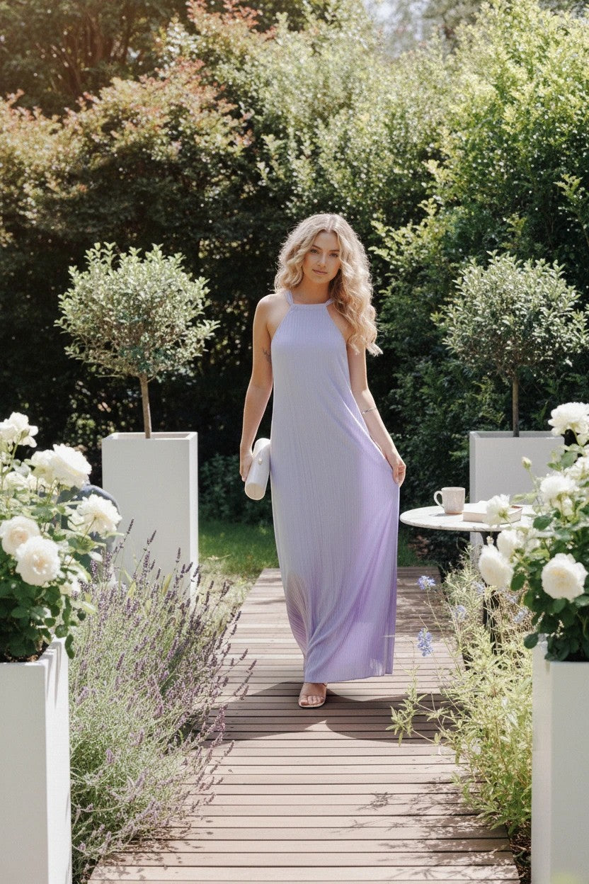 Modèle portant une robe longue Valerelle lavande à col licou dans un jardin fleuri pour un mariage