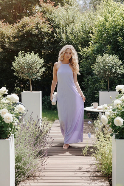 Modèle portant une robe longue Valerelle lavande à col licou dans un jardin fleuri pour un mariage