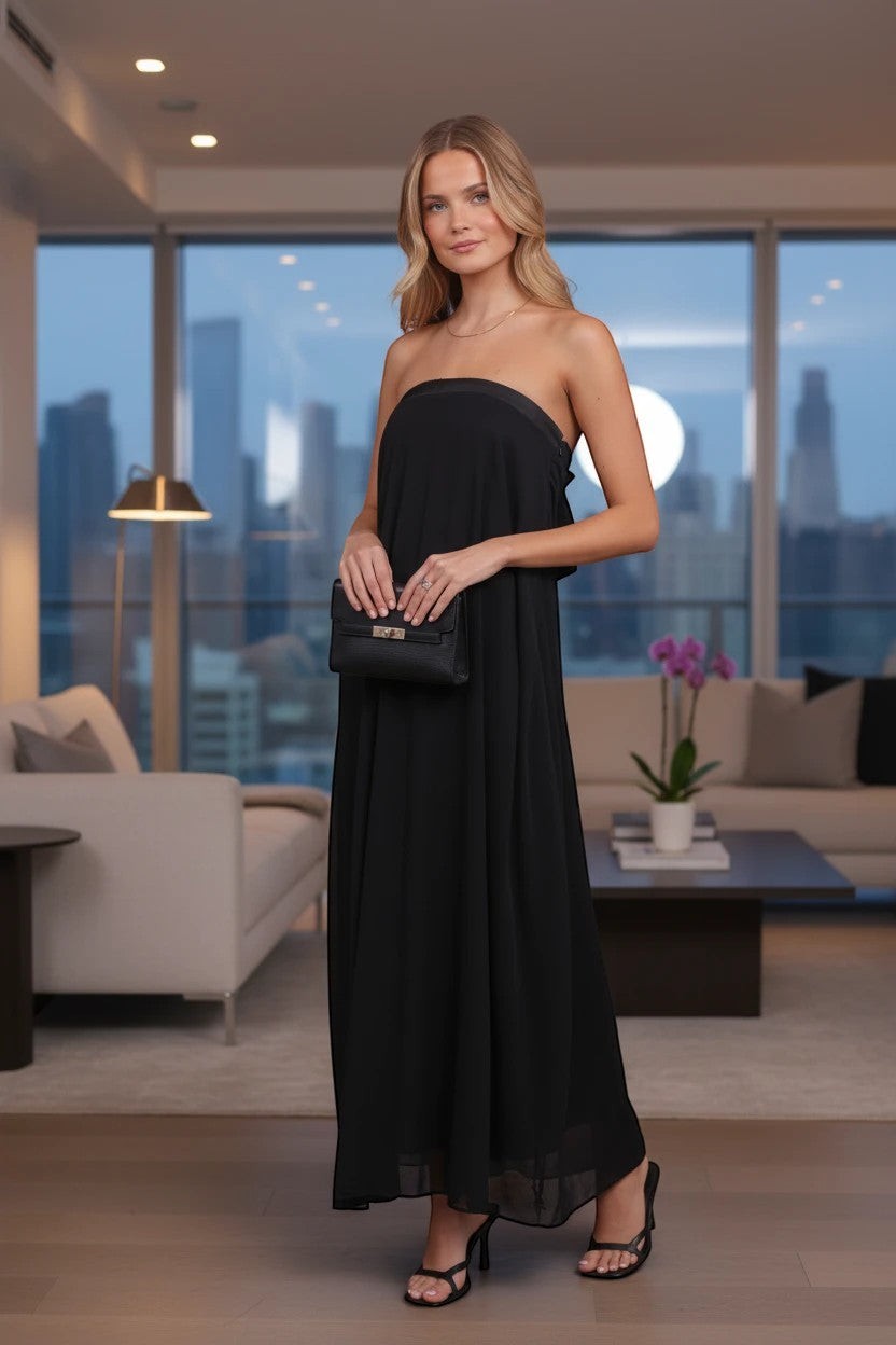 Modèle portant une robe longue Valerelle noire fluide sans bretelles avec une pochette assortie dans un salon chic