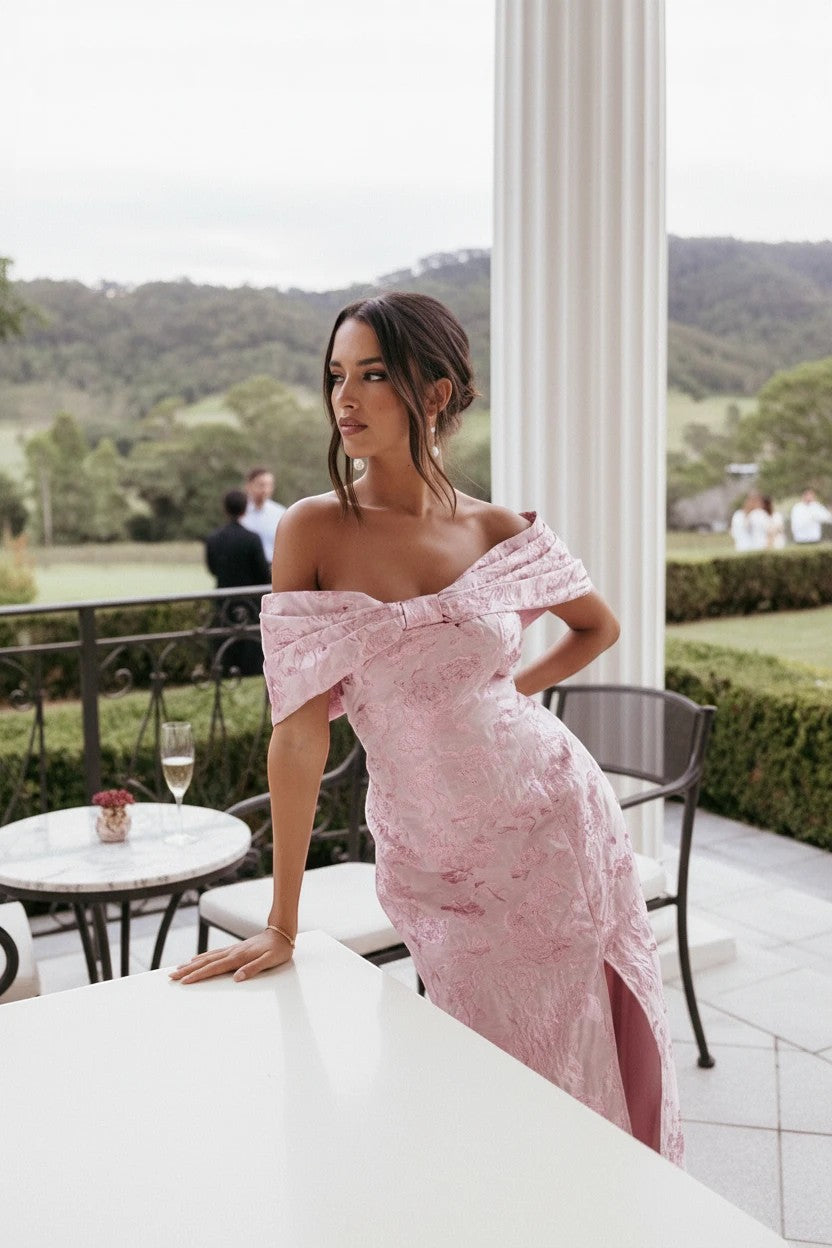 Robe longue Valerelle rose à épaules dénudées et détails texturés, portée par une femme lors d'une réception élégante.