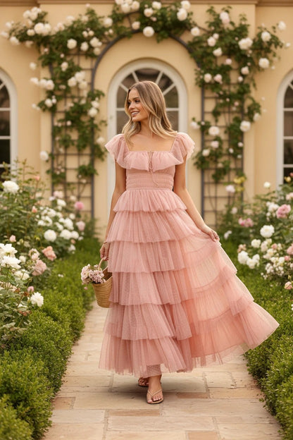 Robe longue Valerelle rose poudré à volants en tulle, portée par une femme dans un jardin fleuri romantique.