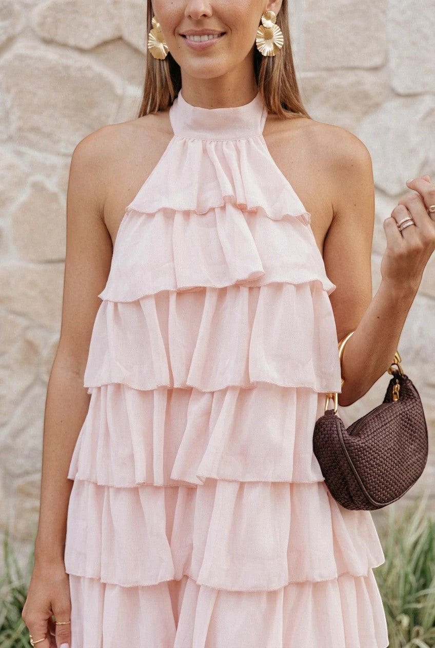 Robe longue Valerelle rose poudré à volants avec col licou, portée par une femme avec des boucles d'oreilles dorées