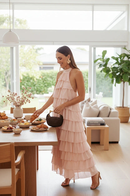 Femme portant une robe longue Valerelle rose poudré à volants avec col licou dans une salle à manger lumineuse