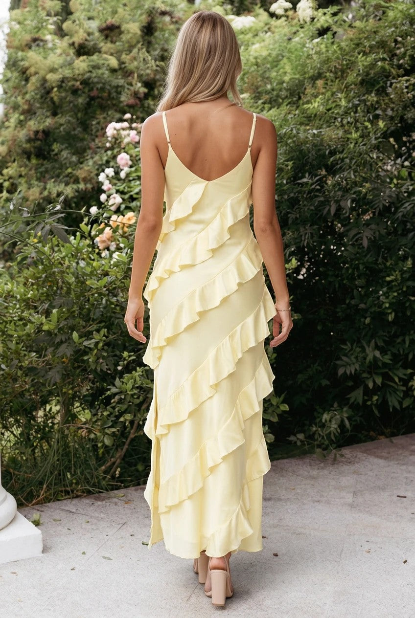 Vue arrière d'une femme portant une robe longue Valerelle jaune en satin avec des volants en cascade dans un jardin