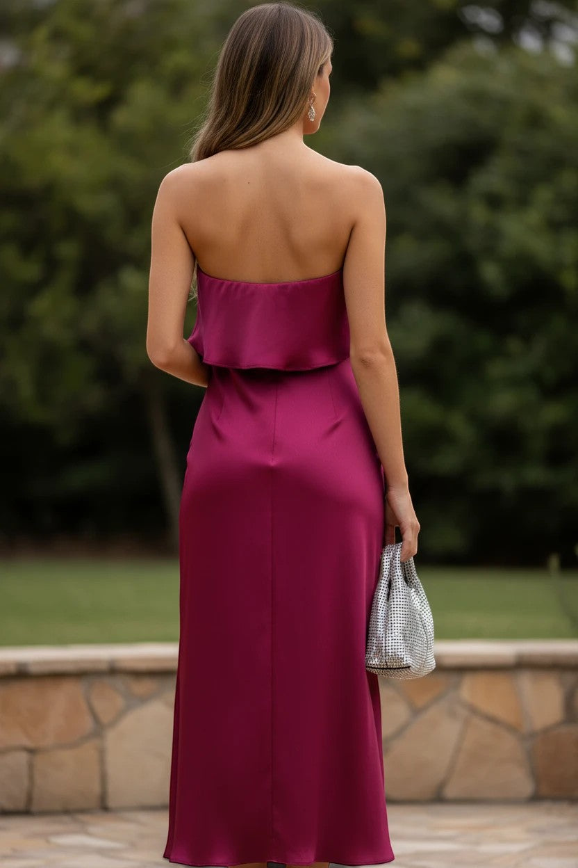 Robe midi bustier Valerelle bordeaux fluide avec dos nu, portée par une femme tenant un sac argenté en extérieur