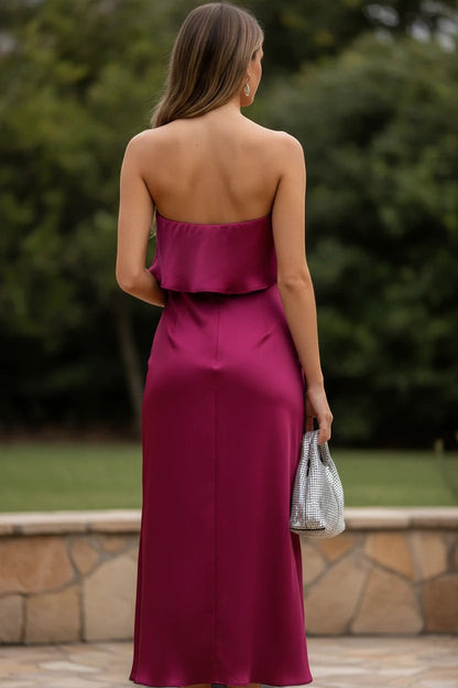 Robe midi bustier Valerelle bordeaux fluide avec dos nu, portée par une femme tenant un sac argenté en extérieur