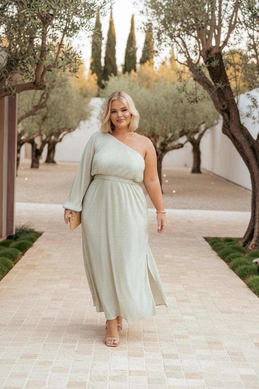 Femme portant une robe midi Valerelle vert sauge plissée asymétrique à une épaule dans un jardin méditerranéen