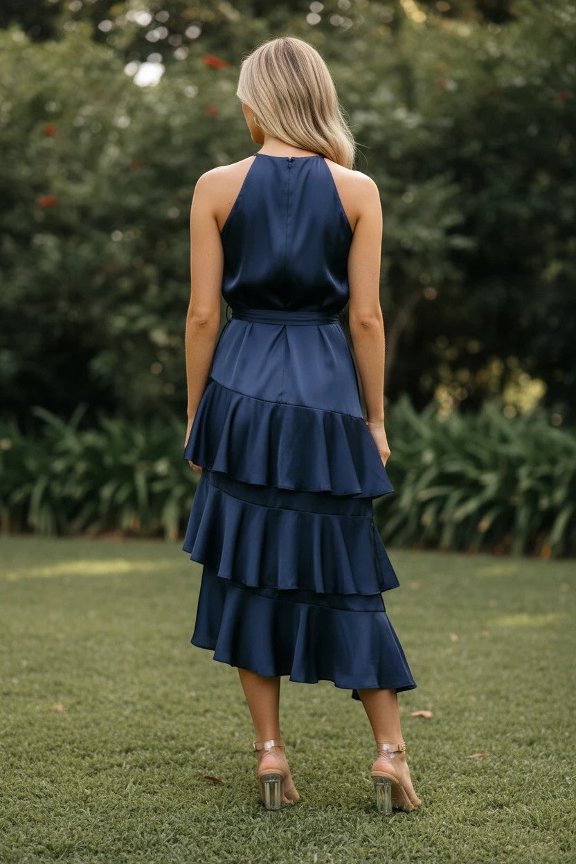 Vue arrière d'une femme portant une robe midi Valerelle bleu nuit en satin avec des volants étagés dans un jardin