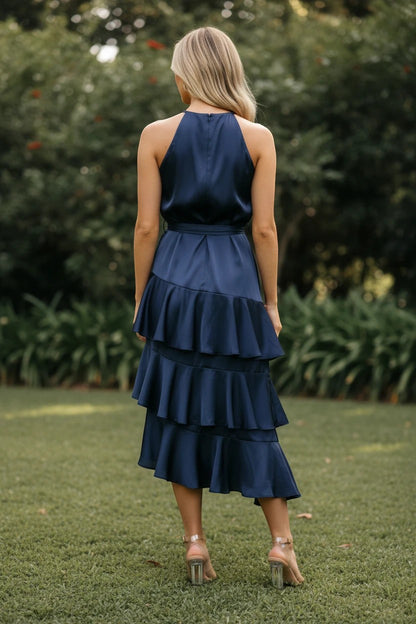 Vue arrière d'une femme portant une robe midi Valerelle bleu nuit en satin avec des volants étagés dans un jardin