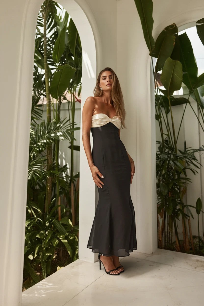Robe de soirée longue Valerelle bustier noir et blanc avec épaules dénudées portée par une femme dans un jardin