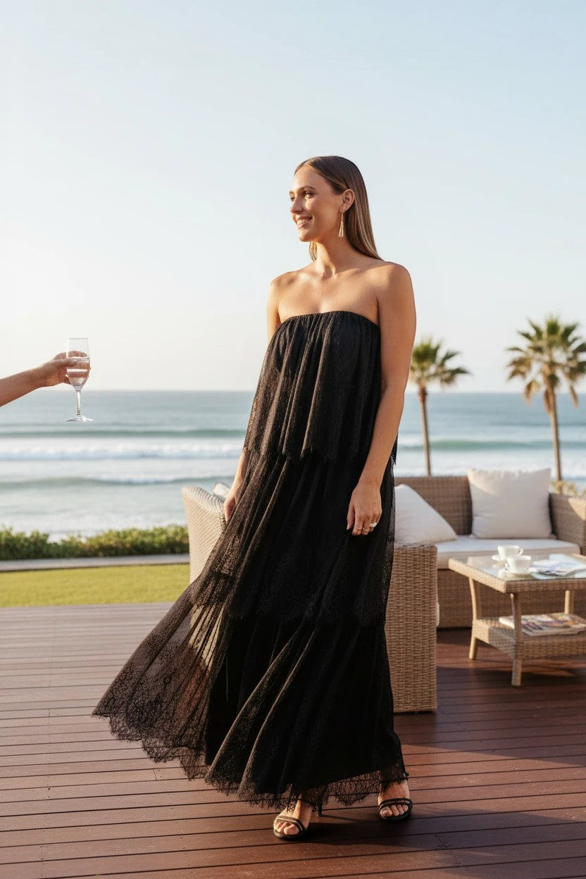 Robe de soirée longue Valerelle en dentelle noire avec bustier sans bretelles portée par une femme sur une terrasse