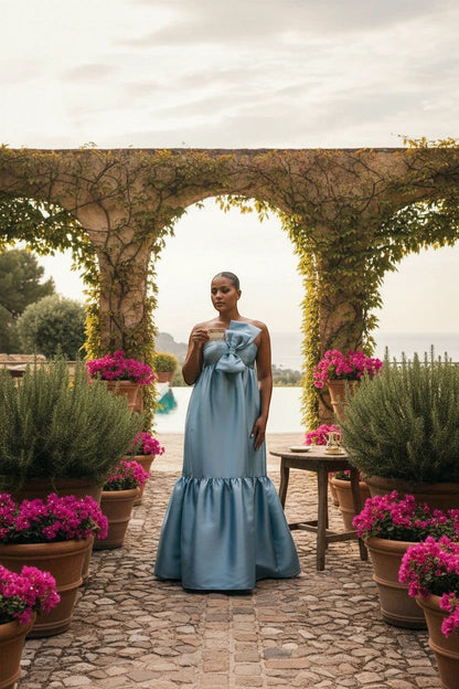 Robe de soirée longue Valerelle bleu profond avec nœud à la taille, portée par une femme dans un jardin méditerranéen.