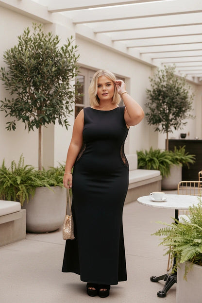 Femme blonde portant une robe de soirée longue noire Valerelle fluide avec détails en dentelle sur les côtés